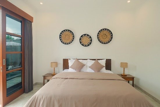 Guest room with a king bed, teak furniture and sliding doors opening onto the pool
